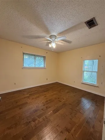 a view of an empty room with wooden floor and a ceiling fan