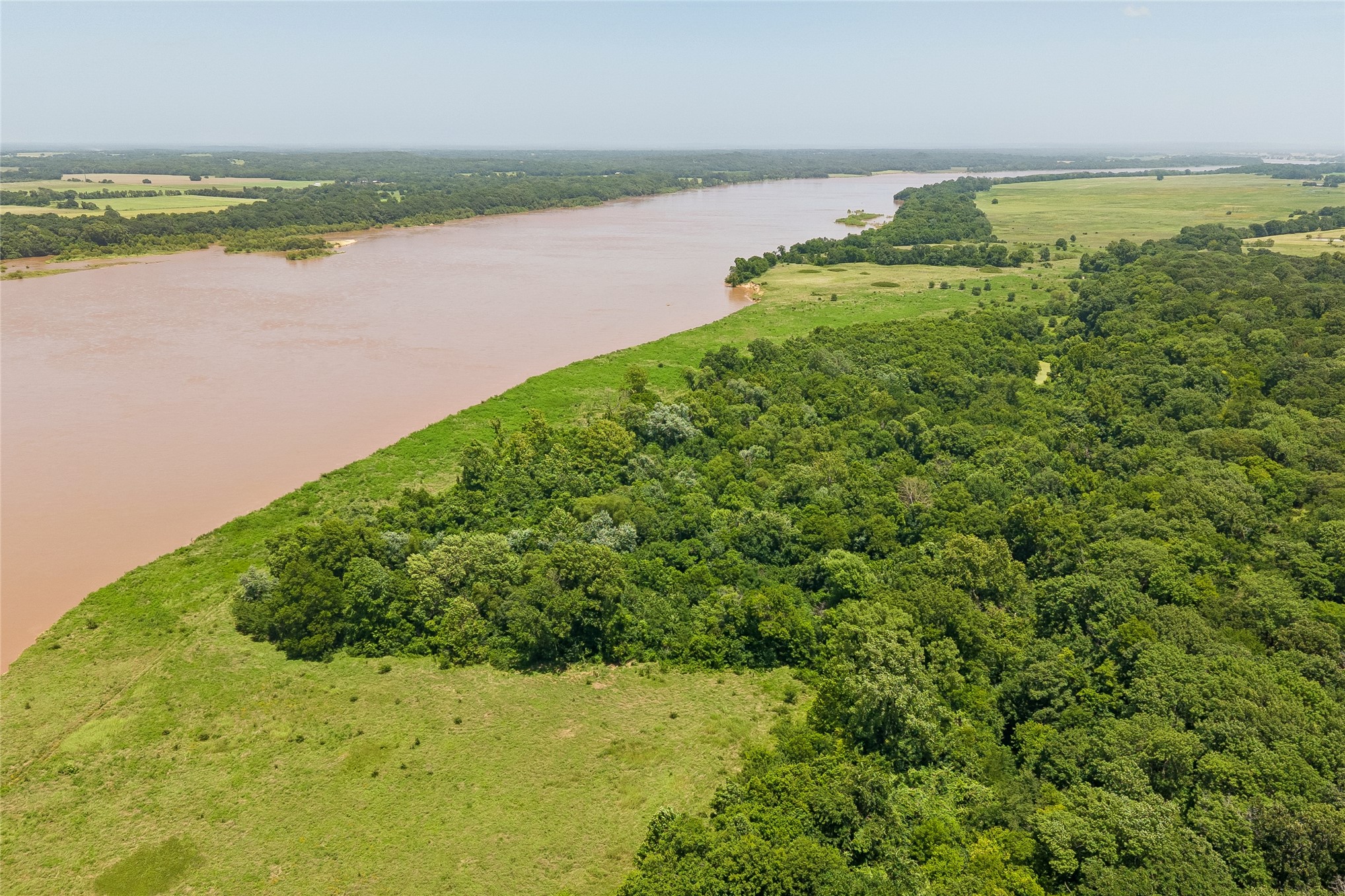Expansive natural landscape featuring a broad river, dense tree lines, and open grassy​​‌​​​​‌​​‌‌​‌‌​​‌​​​​‌​​​‌‌​‌‌‌ areas