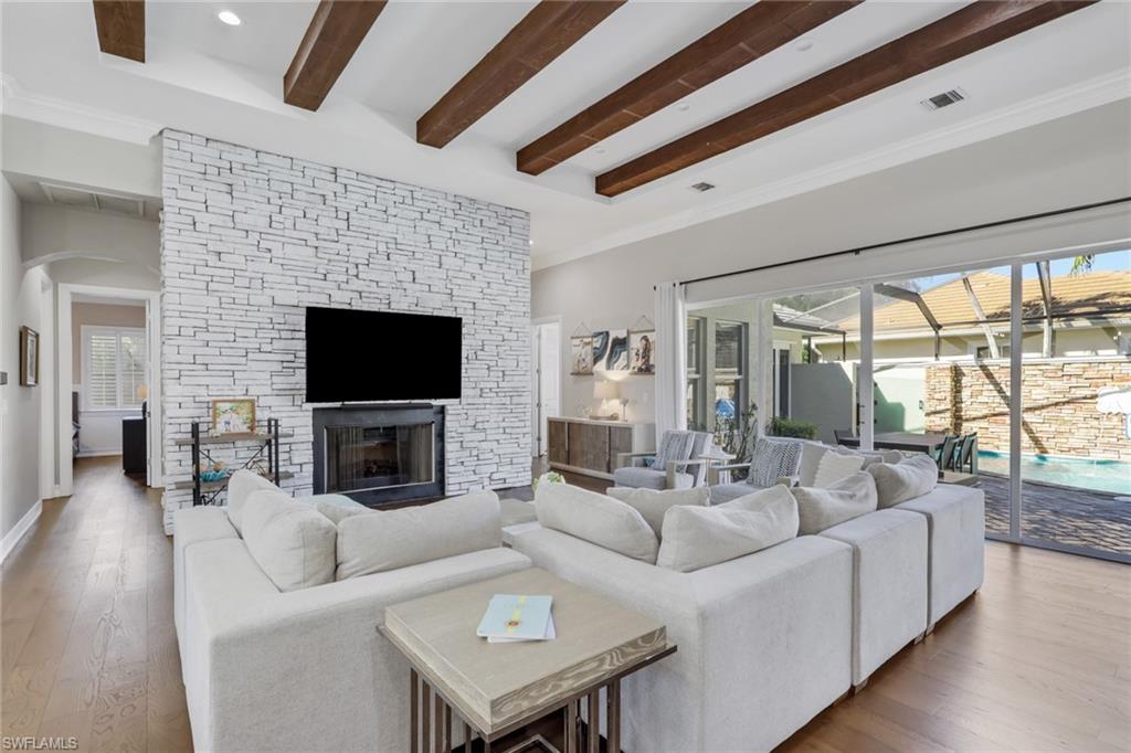 5074 Rustic Oaks Circle Naples, FL 34105 - Photo 13 of 38 Living room featuring hardwood / wood-style floors, beamed ceiling, arched walkways, a sunroom, and a stone fireplace
