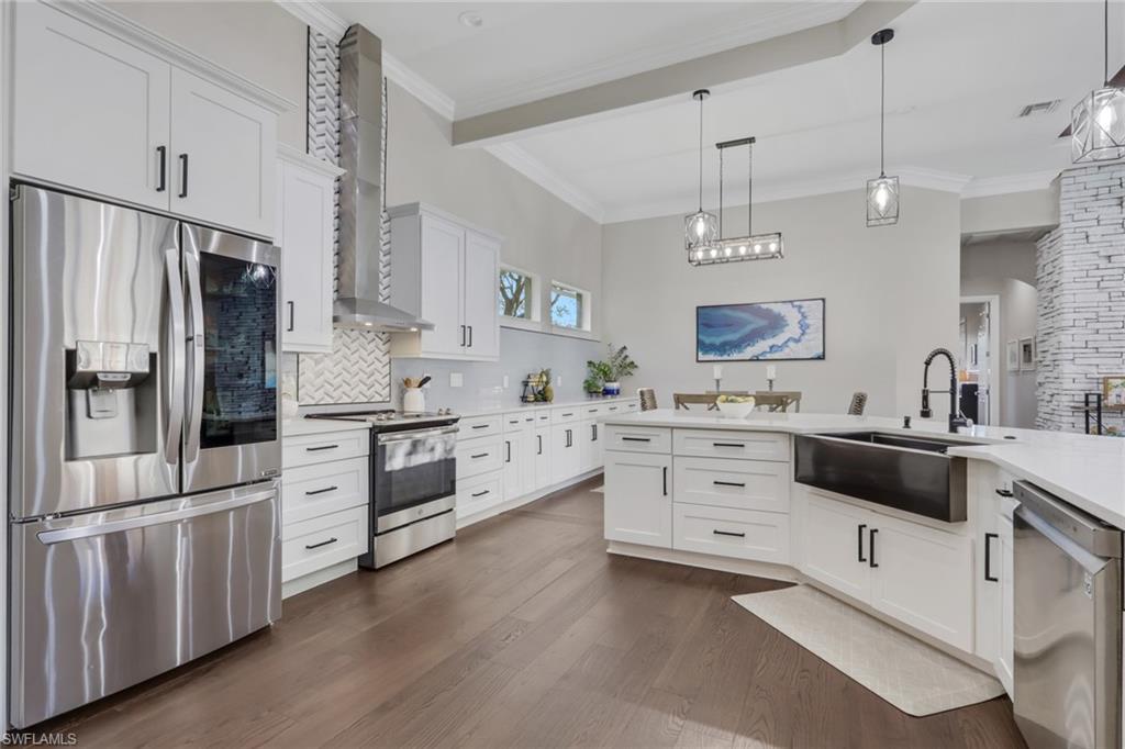 5074 Rustic Oaks Circle Naples, FL 34105 - Photo 7 of 38 Kitchen with stainless steel appliances, white cabinets, decorative light fixtures, wall chimney range hood, and light stone countertops