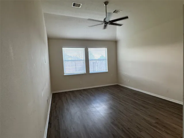 an empty room with wooden floor a ceiling fan and windows