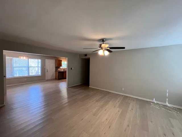 an empty room with wooden floor chandelier fan and windows