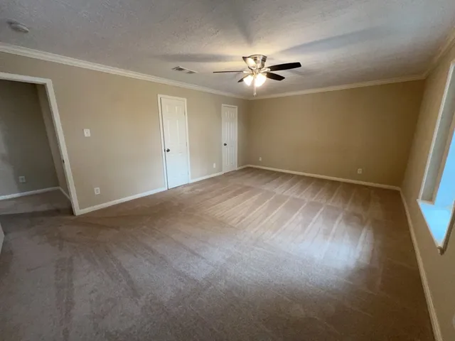 a view of an empty room with wooden floor and fan