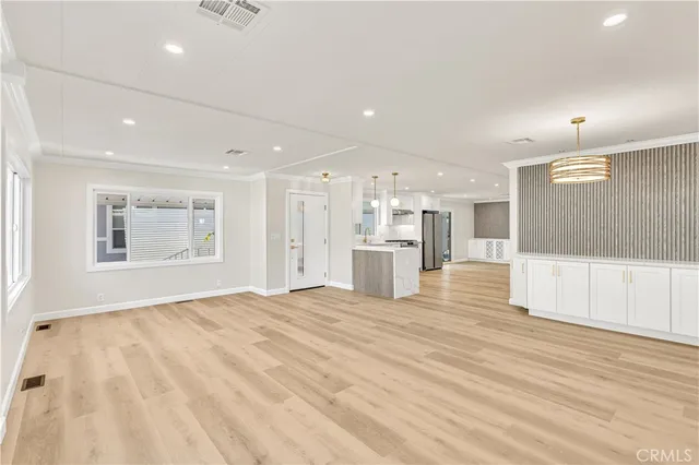 a view of an empty room with wooden floor kitchen view and a window