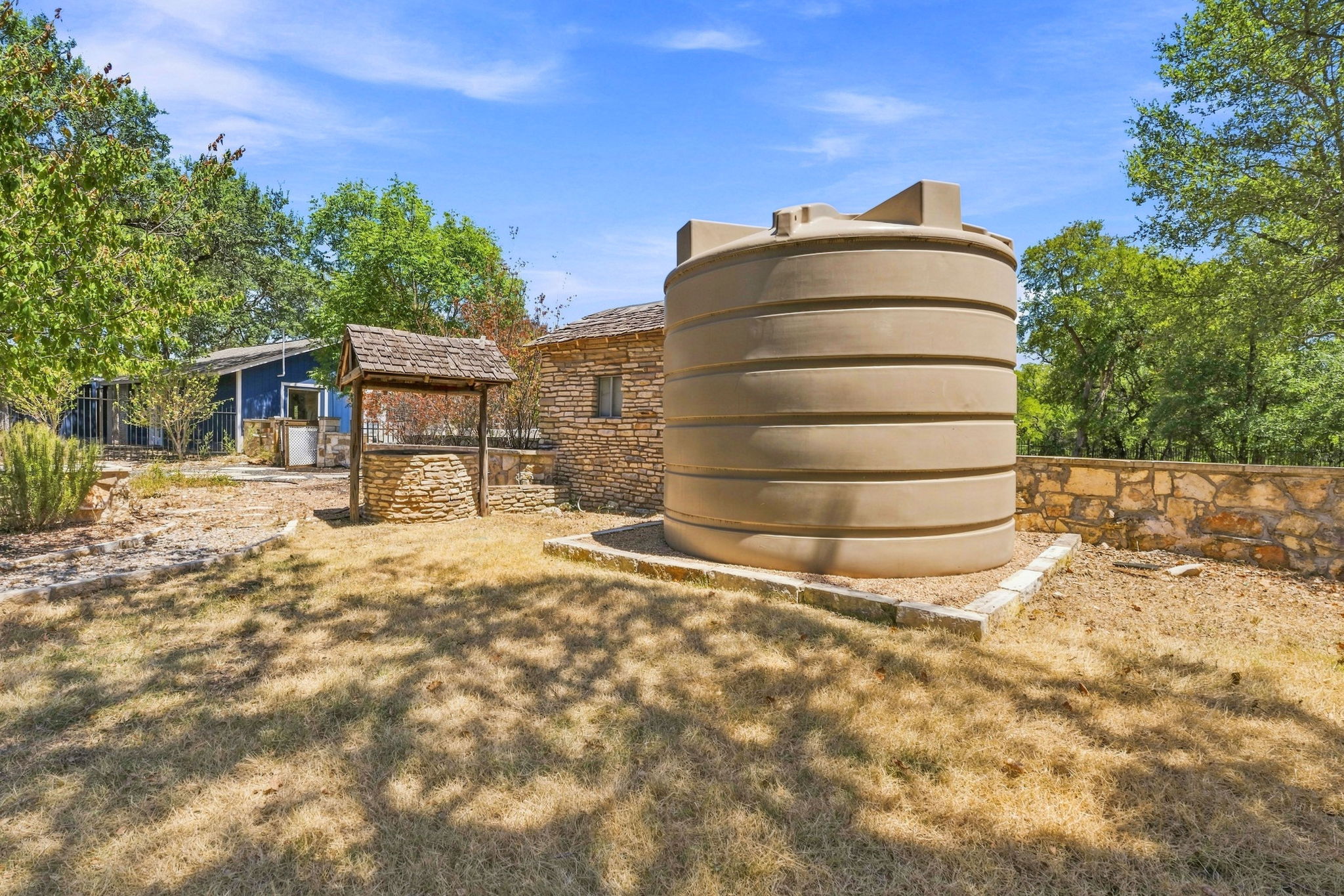 3809 Wyldwood Road Austin, TX 78739 - Photo 28 of 40 Rustic stone outbuildings and a functional water storage tank sit surrounded by mature trees.