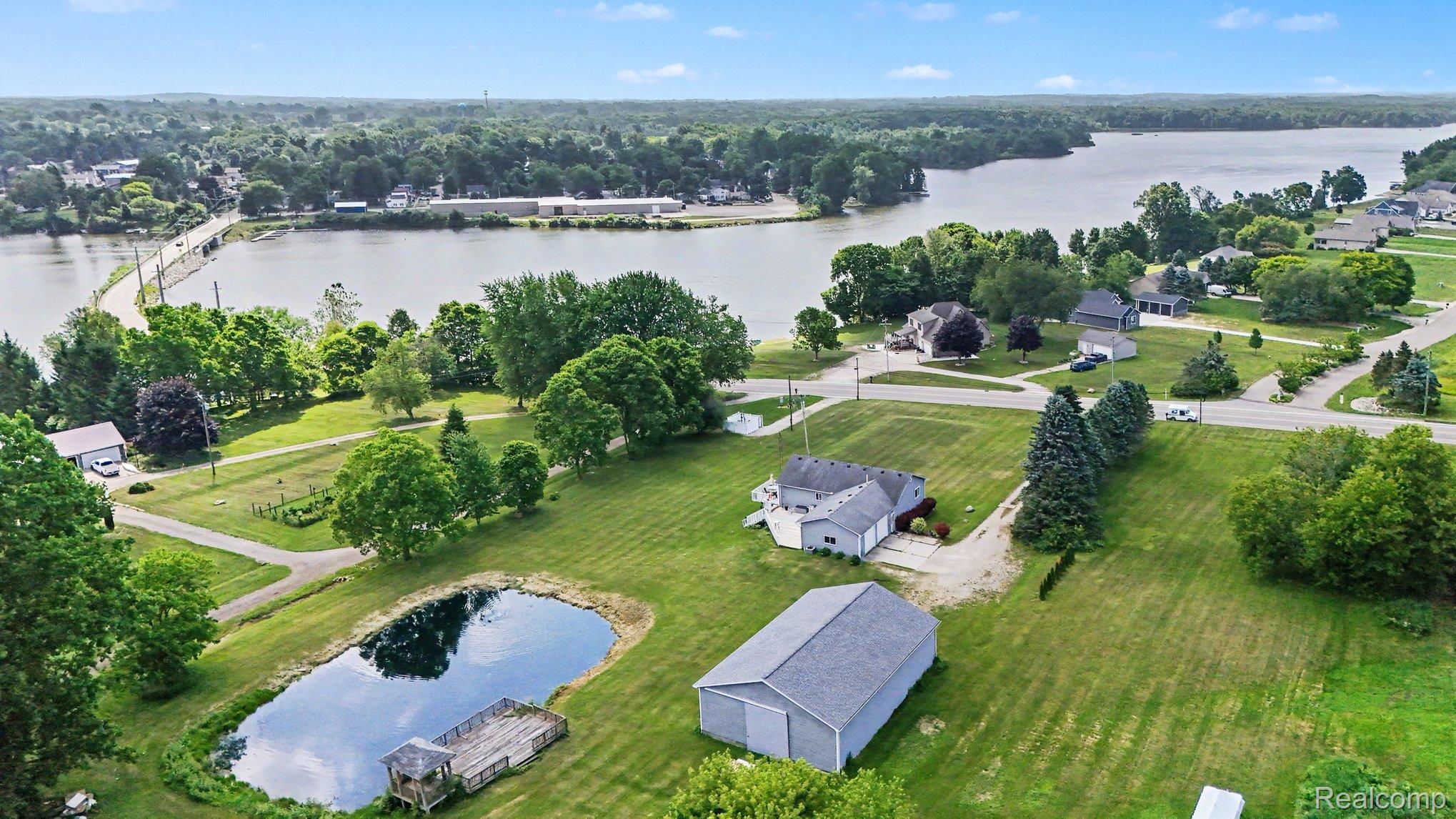 4848 Columbiaville Road Columbiaville, MI 48421 - Photo 29 of 35 Expansive property featuring a private pond with a wooden deck, a detached outbuilding, and a two-story residence with a light gray exterior