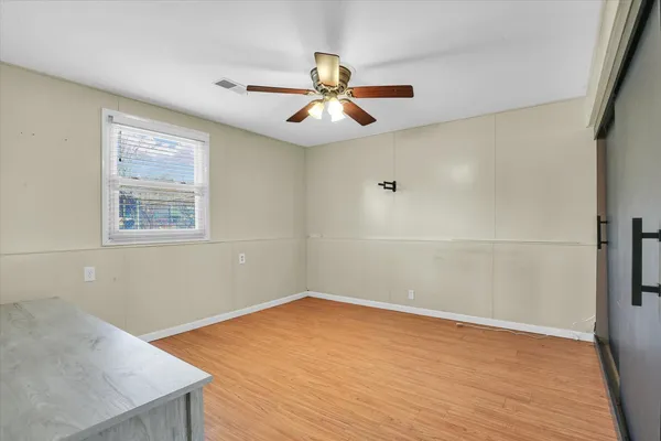 an empty room with wooden floor chandelier fan and windows
