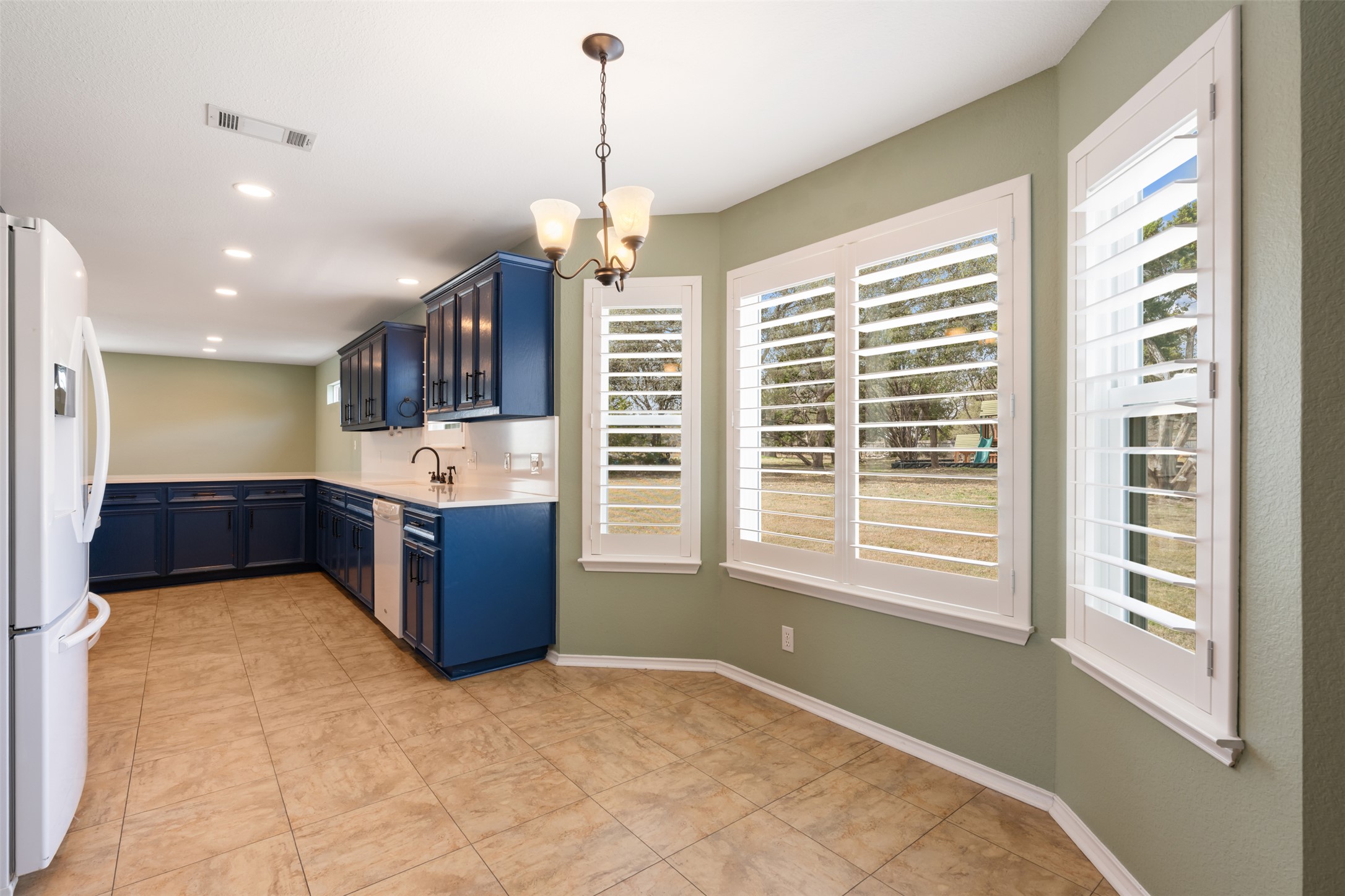 104 Sunset Road Georgetown, TX 78633 - Photo 17 of 40 Kitchen featuring suspended lighting, freestanding refrigerator, blue cabinetry, light tile patterned floors, and light stone counters