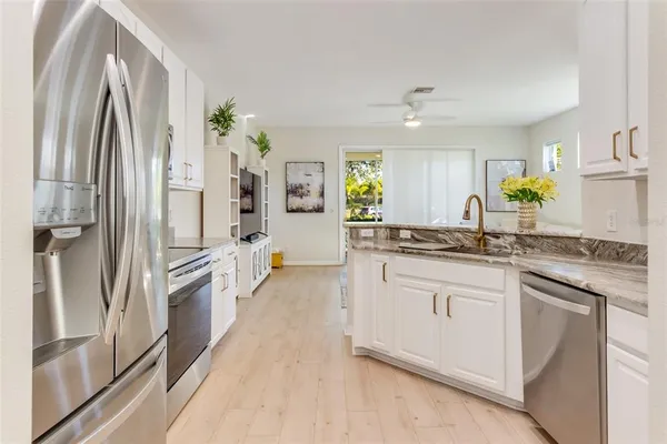 a kitchen with stainless steel appliances granite countertop a refrigerator a sink dishwasher a stove and white cabinets with wooden floor