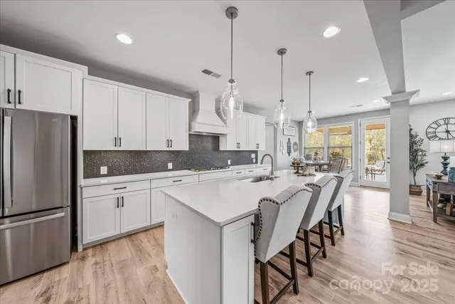 a kitchen with stainless steel appliances granite countertop a refrigerator a sink dishwasher a stove and white cabinets with wooden floor