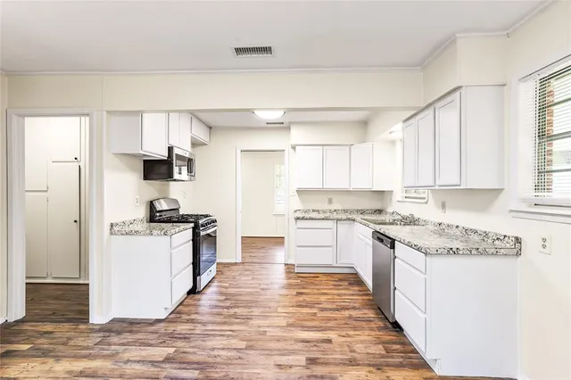 a kitchen with stainless steel appliances granite countertop a stove top oven a sink a refrigerator white cabinets and wooden floor