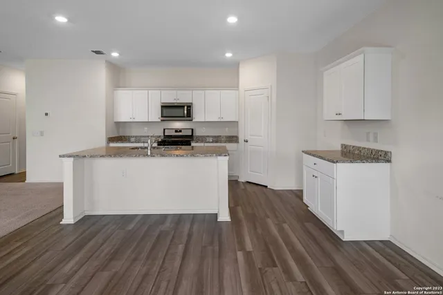 a kitchen with wooden floors white cabinets appliances and a sink