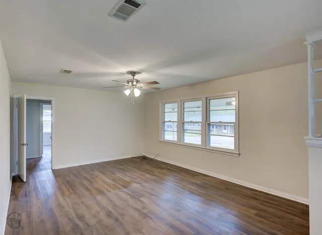 an empty room with wooden floor chandelier fan and windows