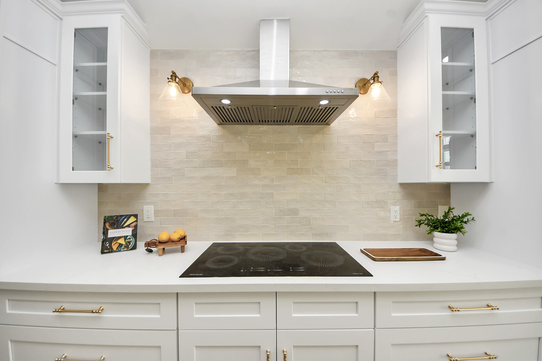 1737 Tabor Street Houston, TX 77009 - Photo 11 of 44 A beautifully curated kitchen where modern white cabinetry with glass accents meets warm brass hardware and soft, ambient lighting. The sleek induction cooktop and stainless steel range hood offer a streamlined look, while a beige subway tile backsplash brings just the right touch of warmth and texture.