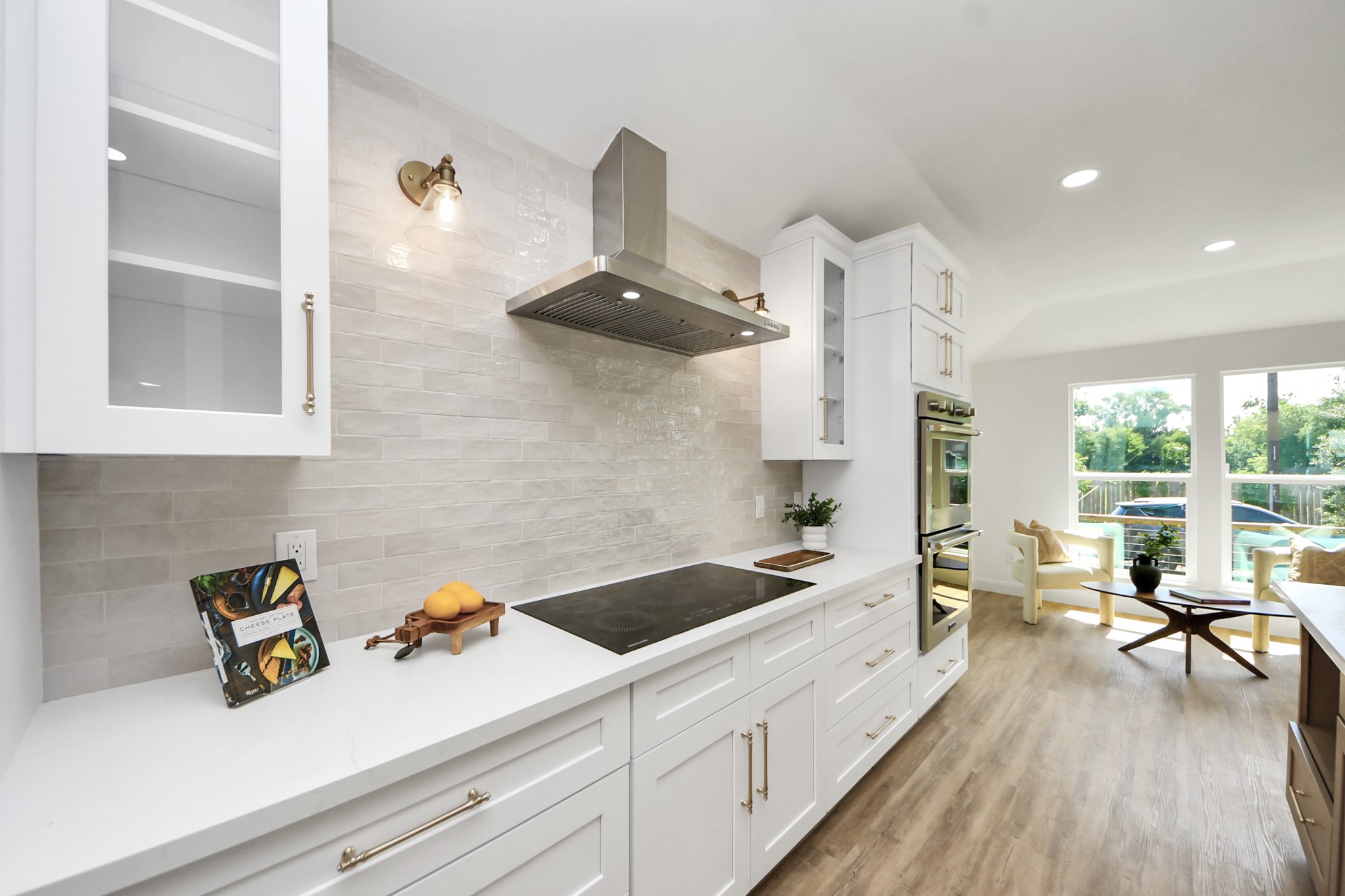 1737 Tabor Street Houston, TX 77009 - Photo 15 of 44 A beautifully curated kitchen where modern white cabinetry with glass accents meets warm brass hardware and soft, ambient lighting. The sleek induction cooktop and stainless steel range hood offer a streamlined look, while a beige subway tile backsplash brings just the right touch of warmth and texture.