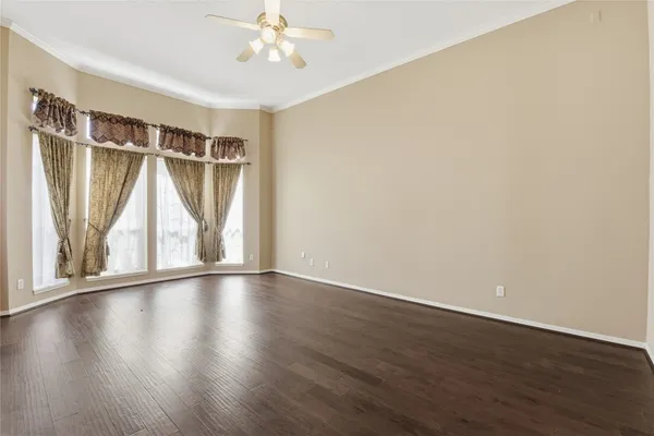 an empty room with wooden floor chandelier fan and windows