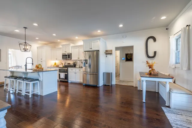 a open kitchen with stainless steel appliances granite countertop a stove top oven a sink dishwasher a dining table and chairs with wooden floor