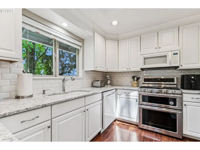 a kitchen with granite countertop a stove a sink and white cabinets