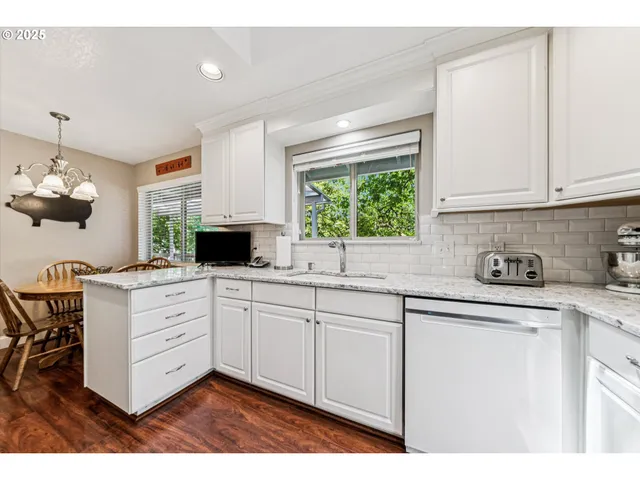 a kitchen with granite countertop white cabinets white appliances a sink and a large window