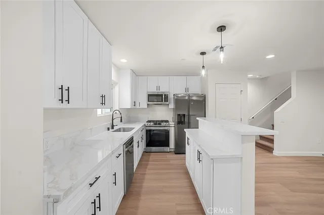 a large kitchen with stainless steel appliances kitchen island granite countertop a stove a sink a refrigerator and white cabinets with wooden floor