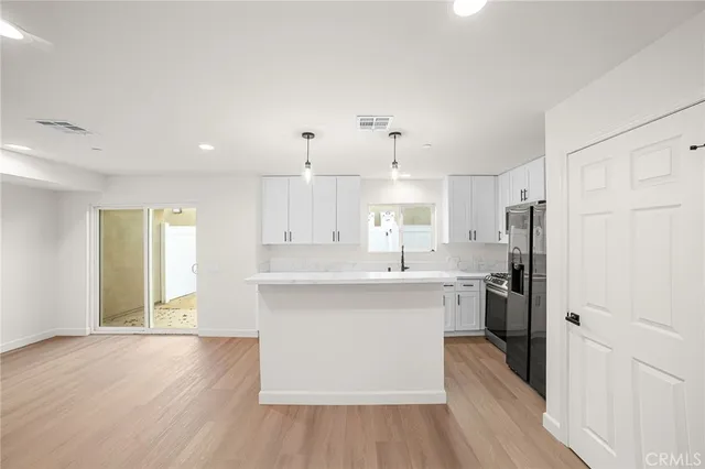 a kitchen with stainless steel appliances granite countertop a refrigerator a sink dishwasher a stove and white countertops with wooden floor