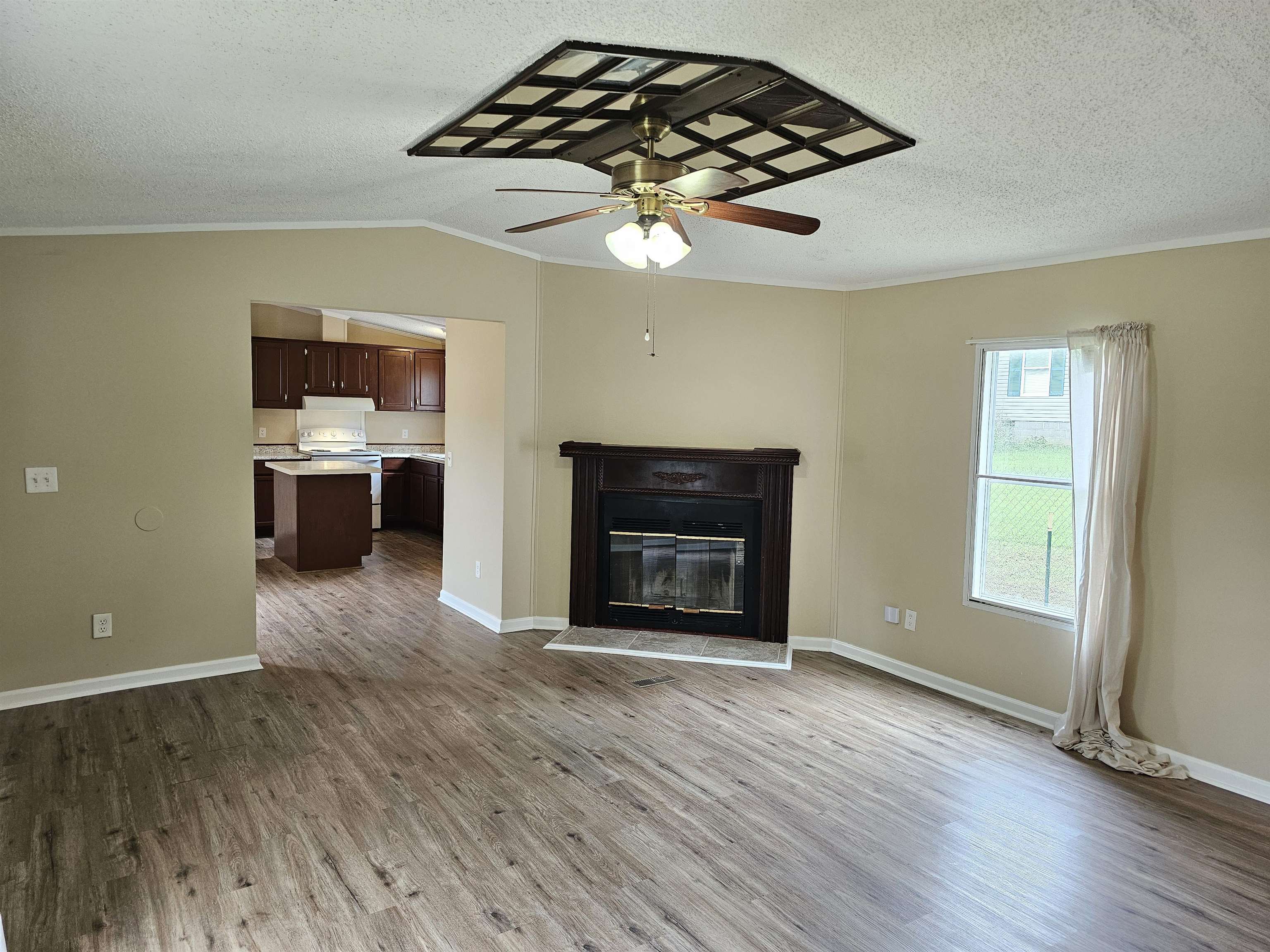 474 Fite Road Munford, TN 38058 - Photo 11 of 19 Unfurnished living room featuring a glass covered fireplace, crown molding, wood finished floors, a textured ceiling, and ceiling fan