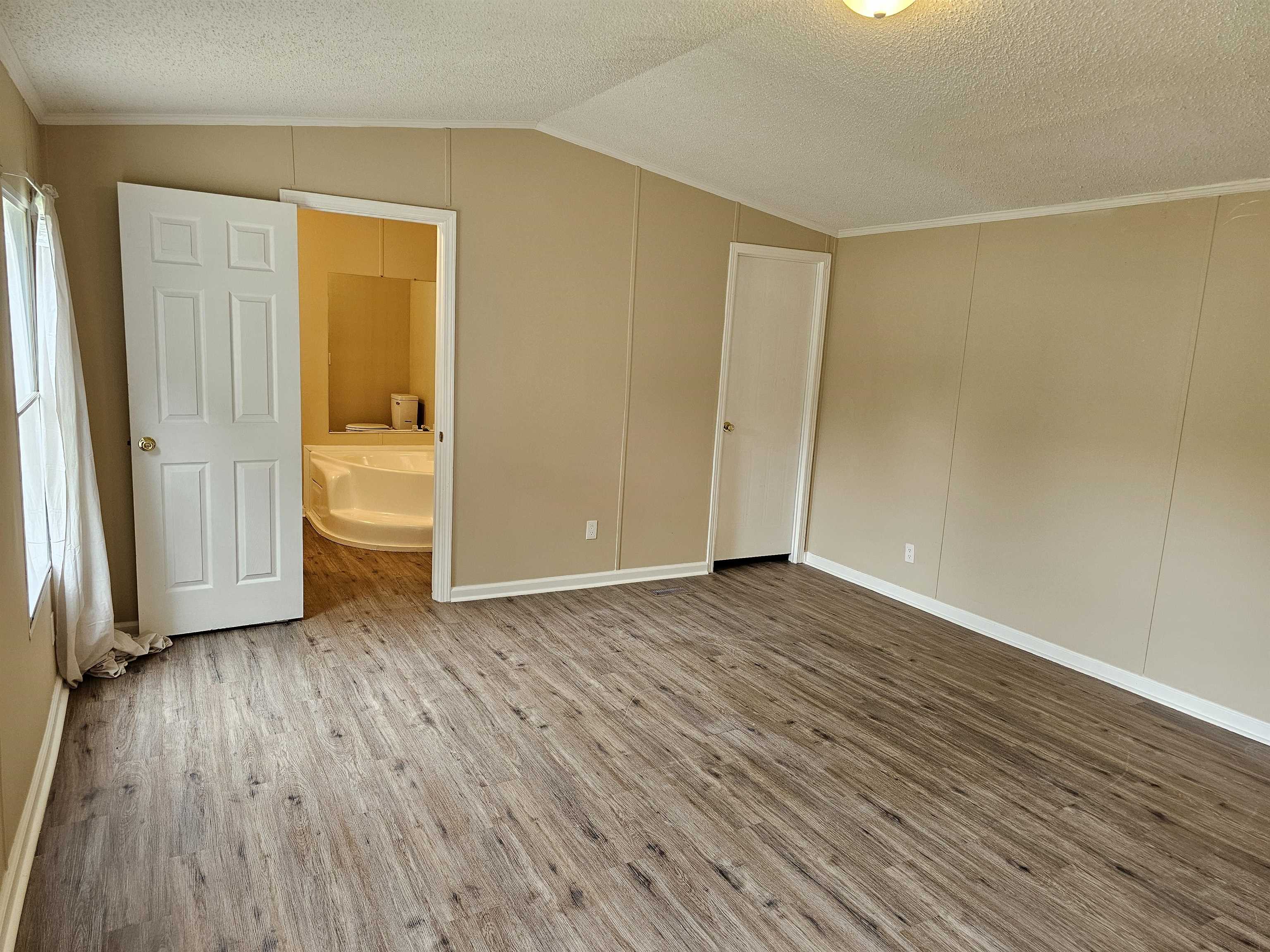 474 Fite Road Munford, TN 38058 - Photo 7 of 19 Unfurnished bedroom with lofted ceiling, a textured ceiling, wood finished floors, ornamental molding, and a decorative wall