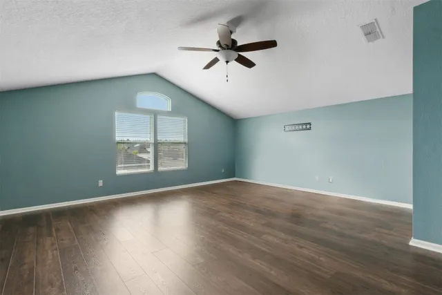 an empty room with wooden floor chandelier fan and windows