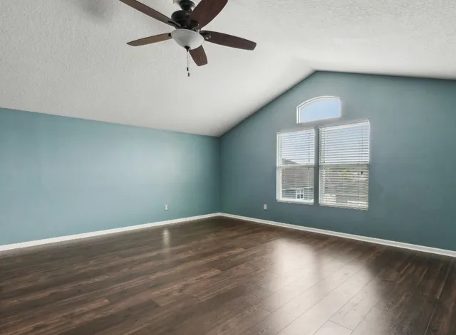 an empty room with wooden floor fan and windows