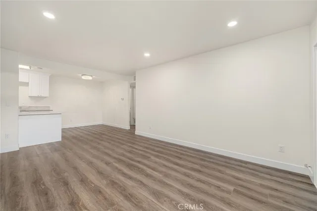 a view of an empty room with wooden floor and a kitchen