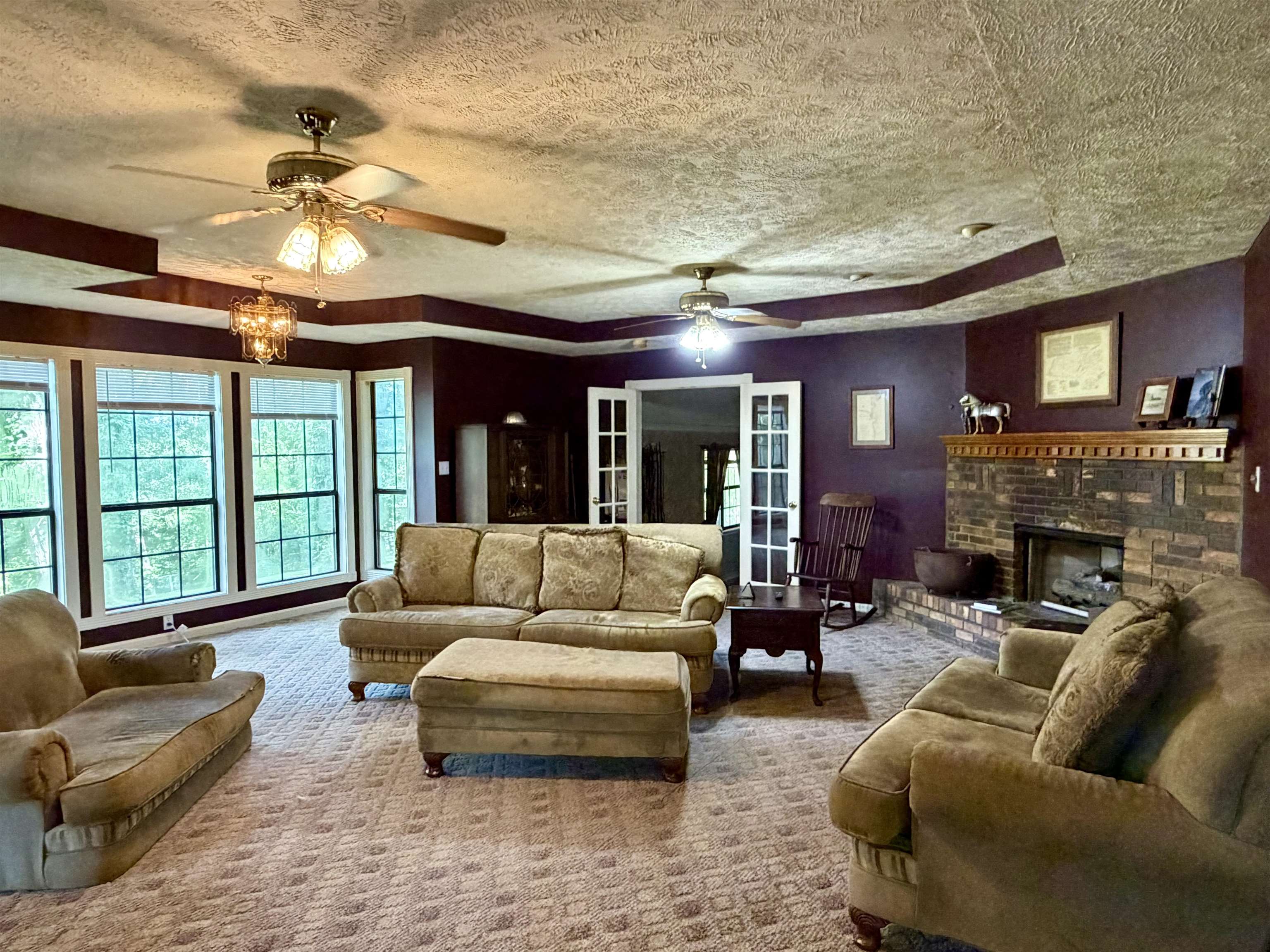 373 Clarence Barham Road Bethel Springs, TN 38315 - Photo 2 of 28 Spacious living area featuring a prominent brick fireplace with a wood mantle, multiple ceiling fans, and recessed tray ceiling details