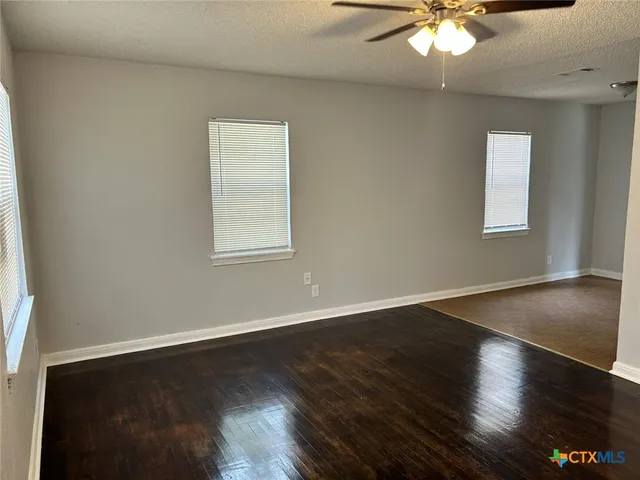 an empty room with wooden floor chandelier fan and windows