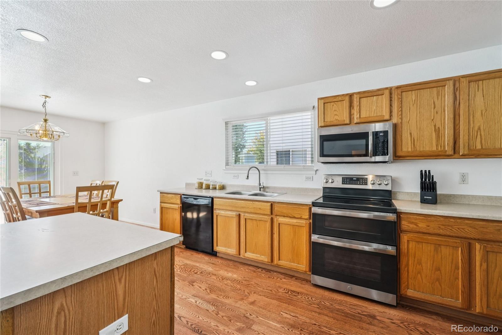 9230 Cook Street Thornton, CO 80229 - Photo 11 of 34 a kitchen with stainless steel appliances granite countertop a stove top oven a sink dishwasher a dining table and chairs with wooden floor