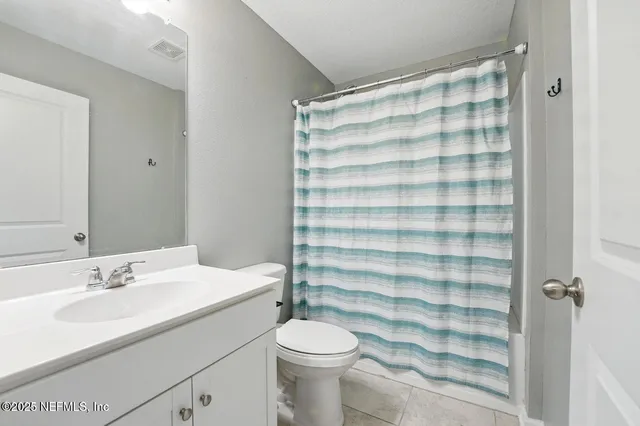 a bathroom with a sink a toilet a shower curtain and a large mirror