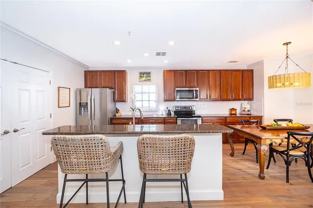 a kitchen with stainless steel appliances kitchen island granite countertop a dining table chairs and a refrigerator
