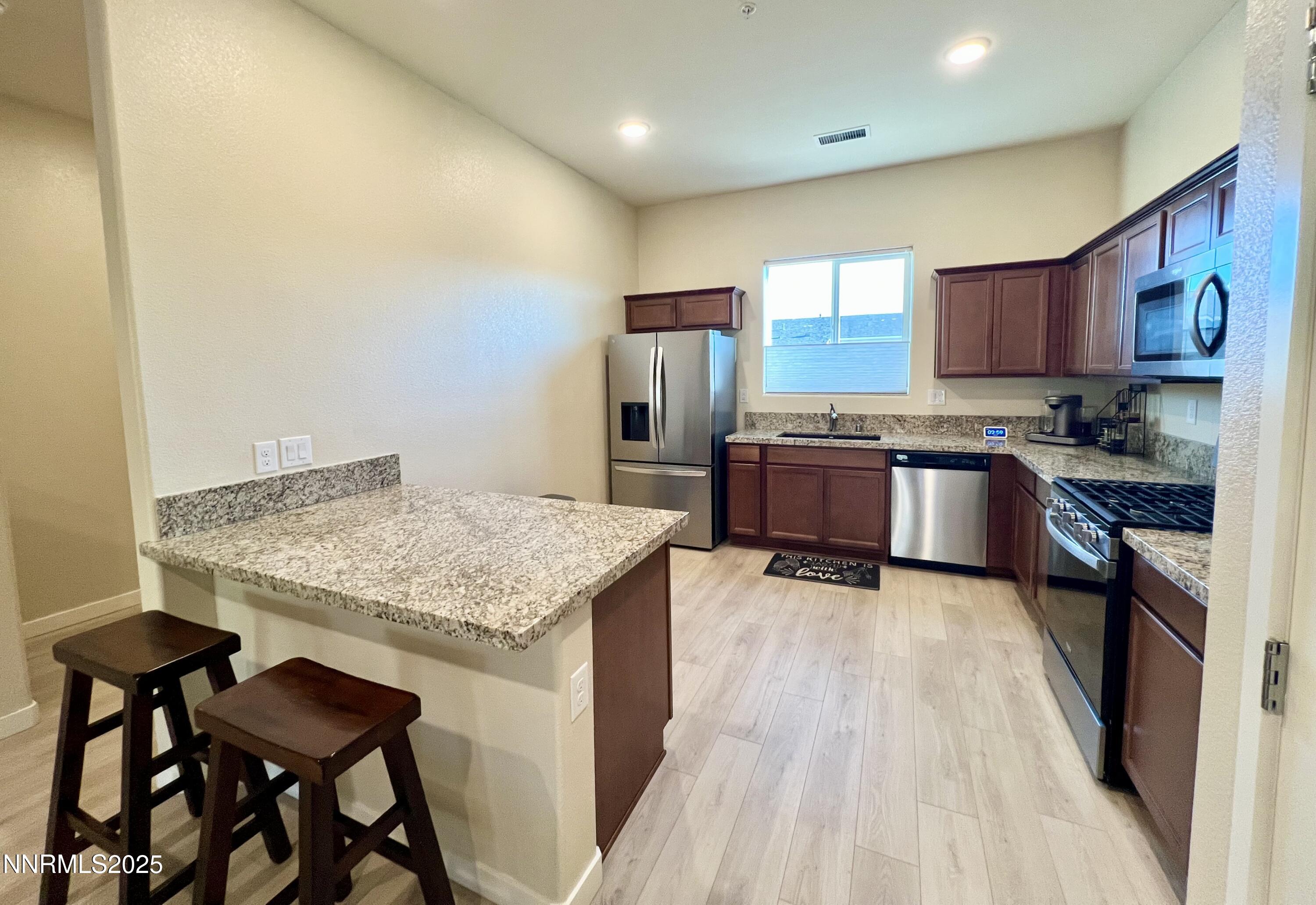 4969 Cavestone Road Sun Valley, NV 89433 - Photo 10 of 40 a kitchen with stainless steel appliances granite countertop a stove top oven a sink dishwasher and a refrigerator with wooden floor