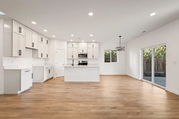 a large white kitchen with kitchen island a sink wooden floor and a large window