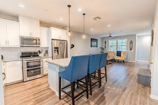 a kitchen with stainless steel appliances kitchen island granite countertop a table chairs and a refrigerator