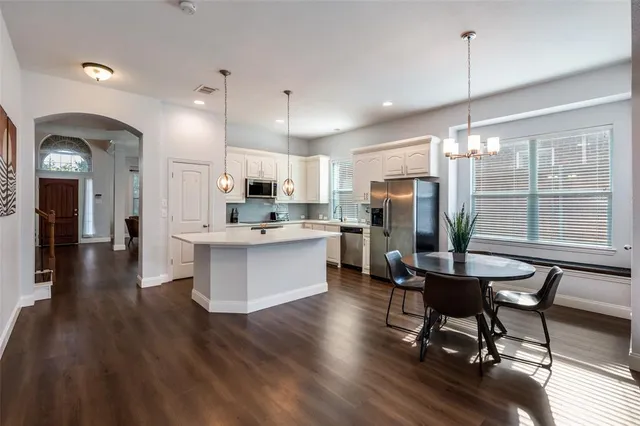 a kitchen with stainless steel appliances kitchen island granite countertop a refrigerator a stove a kitchen island a dining table and chairs with wooden floor