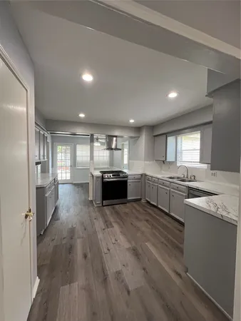 a large white kitchen with a stove a sink dishwasher and a refrigerator with wooden floor