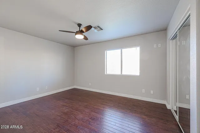 an empty room with wooden floor ceiling fan and windows