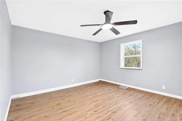 an empty room with wooden floor ceiling fan and windows