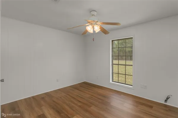 an empty room with wooden floor fan and windows