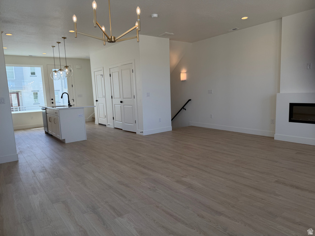 10995 South Freestone Road, Unit 109 South Jordan, UT 84009 - Photo 8 of 20 Unfurnished living room with a chandelier, light wood finished floors, and a glass covered fireplace