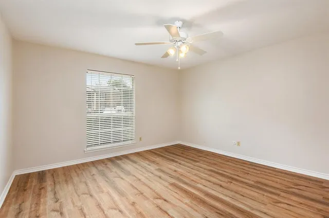 an empty room with wooden floor fan and windows
