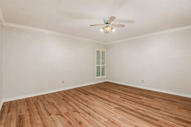 a view of an empty room with wooden floor and a fan