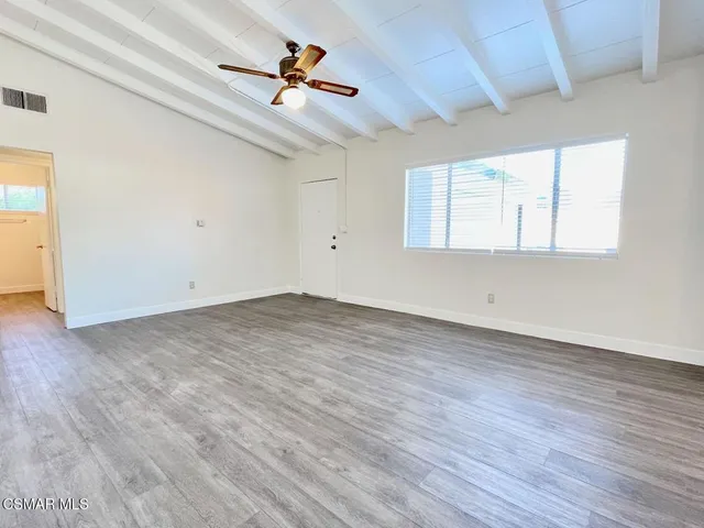 an empty room with wooden floor chandelier fan and windows