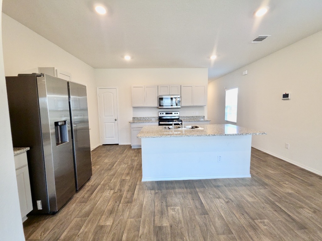 13525 Open Wagon Trail Elgin, TX 78621 - Photo 8 of 26 Kitchen featuring stainless steel appliances, light stone counters, a center island with sink, dark wood-style floors, and recessed lighting