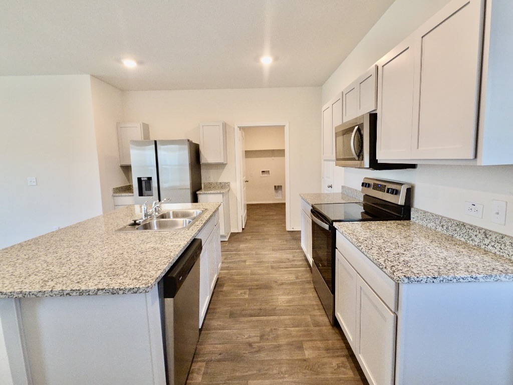 13525 Open Wagon Trail Elgin, TX 78621 - Photo 9 of 26 Kitchen with stainless steel appliances, white cabinetry, dark wood-style floors, a kitchen island with sink, and light stone countertops