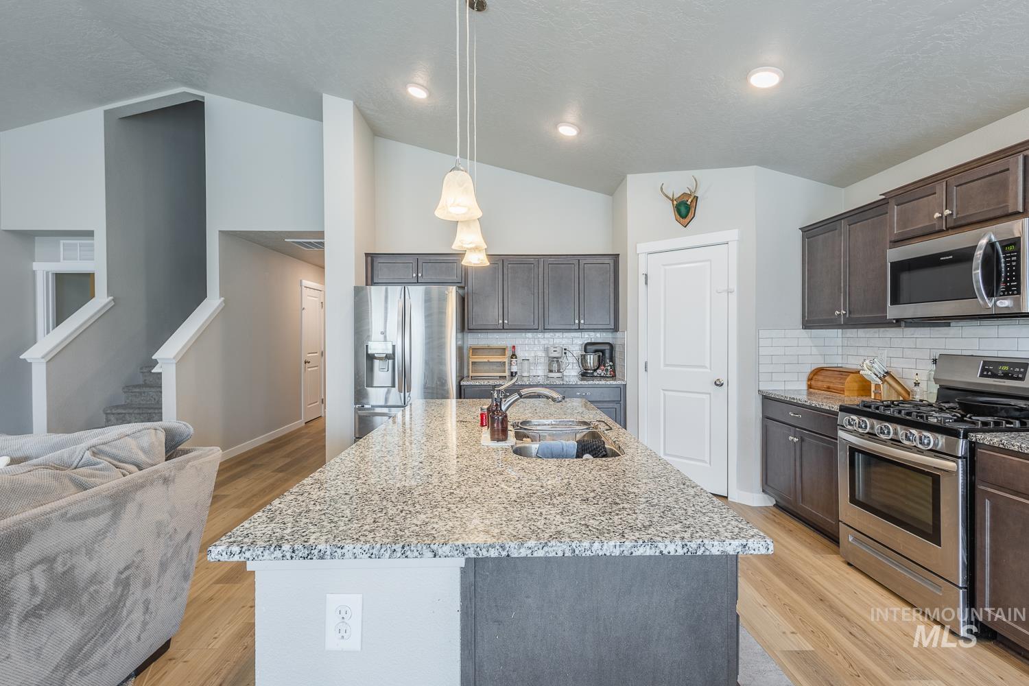 12623 Shadow Peak Street Caldwell, ID 83607 - Photo 15 of 50 Open concept kitchen featuring an expansive island with a sink, pendant lighting, stainless steel appliances, dark wood-finish cabinetry, and a white subway tile backsplash
